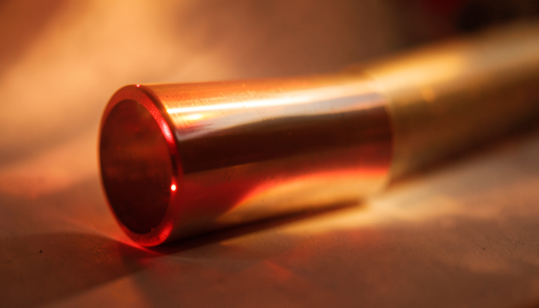 Tube métallique poli sous éclairage de laboratoire, avec des reflets chauds sur sa surface cylindrique.